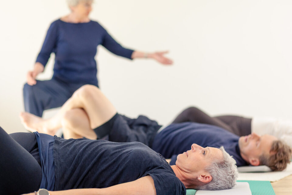 Die Teilnehmer der physiotherapeutischen Kurse liegen auf dem Boden und machen eine Übung | Physiotherapie Schmeddes