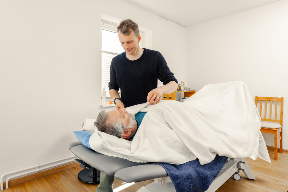 Ein Herr wird bei der Fango Therapie in warme Wickel eingewickelt | Physiotherapie Schmeddes